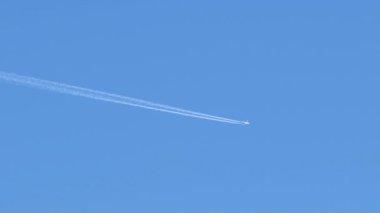 Mesafeli yolcu jet uçağı açık mavi gökyüzünde yüksek irtifada uçarken ardında beyaz duman izi bırakıyor. Hava taşımacılığı kavramı
