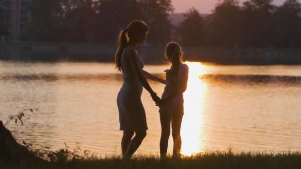 Счастливые мама и дочка расслабляются, держась за руки, наслаждаясь временем вместе в летнем парке на закате. Концепция семейной любви и отношений — стоковое видео
