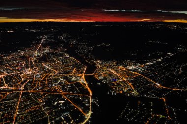 Uçak penceresinden gökyüzü manzarası ve şehrin yerleşim alanındaki aydınlık sokaklar. Yüksek irtifada karanlık şehir manzarası