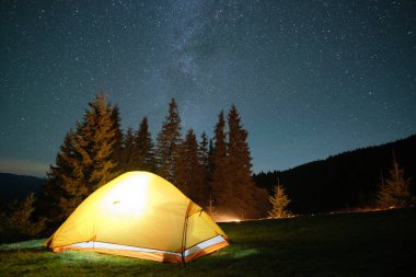 Parlak turist çadırı gece gökyüzünün altındaki karanlık dağlarda parlayan yıldızlarla parlıyordu. Etkin yaşam tarzı kavramı