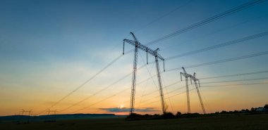Güneş doğarken elektrik hatları olan yüksek voltajlı kulelerin koyu gölgesi.
