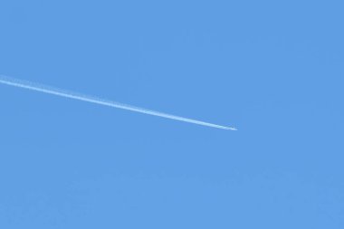 Mesafeli yolcu jet uçağı açık mavi gökyüzünde yüksek irtifada uçarken ardında beyaz duman izi bırakıyor. Hava taşımacılığı kavramı