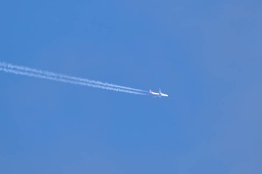 Mesafeli yolcu jet uçağı açık mavi gökyüzünde yüksek irtifada uçarken ardında beyaz duman izi bırakıyor. Hava taşımacılığı kavramı