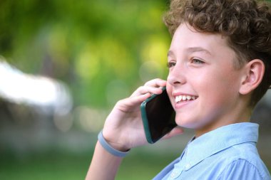 Yazlık parkta cep telefonuyla konuşan mutlu genç bir çocuk. Çevrimiçi arkadaşlık kavramı