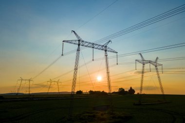Gün batımında elektrik hatları olan yüksek voltaj kuleleri.