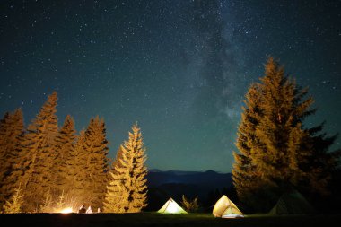 Parlak şenlik ateşinin yanında dinlenen yürüyüşçüler parlayan yıldızlarla dolu karanlık dağ ormanlarındaki kamp alanlarında kamp yapıyorlar. Aktif yaşam tarzı ve açık hava yaşam konsepti