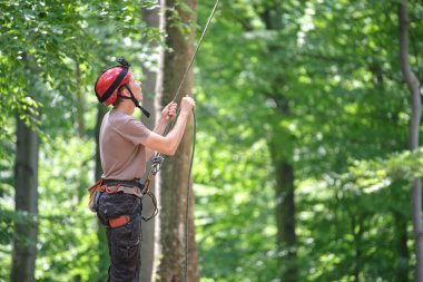 Adam bağlanma cihazı ve iple ortağını bağlıyor. Tırmanışçılar kaya dağcılığı güvenliği için ekipman tutuyor.