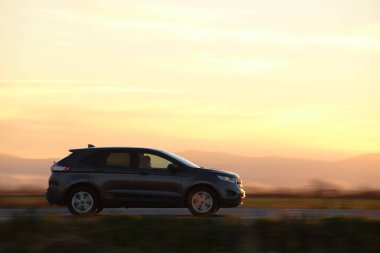 Gün batımında şehirlerarası yolda hızla giden bir SUV arabası. Akşamları otoyol trafiği