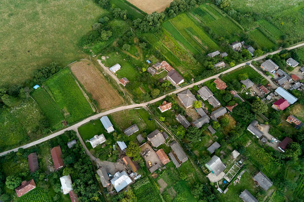 Aerial landscape view of village houses and distant green cultivated agricultural fields with growing crops on bright summer day