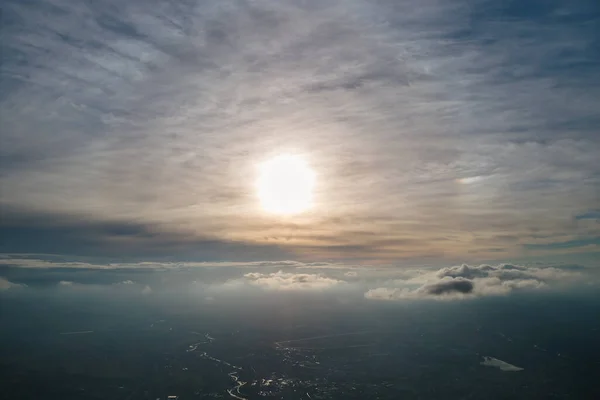Luftaufnahme aus dem Flugzeugfenster in großer Höhe der Erde, bedeckt mit einer weißen dünnen Nebelschicht und fernen Wolken bei Sonnenuntergang — Stockfoto