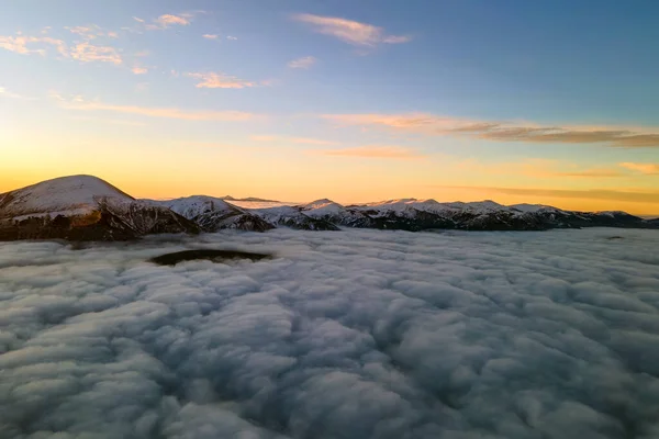 水平線に遠くの暗い山と白い高密度の雲の上の鮮やかな日の出の空中ビュー — ストック写真