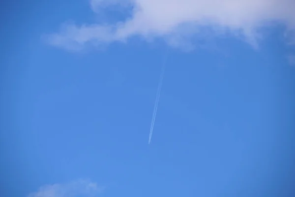 Avión a reacción de pasajeros lejano volando a gran altitud en el cielo azul con nubes blancas dejando rastro de humo de la estela detrás. Concepto de viaje aéreo — Foto de Stock