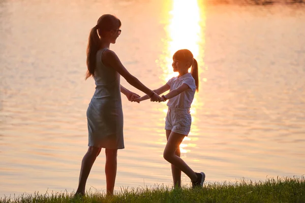 Χαρούμενη μαμά και κόρη κορίτσι χαλαρωτικό κρατώντας τα χέρια απολαμβάνοντας το χρόνο μαζί στο καλοκαιρινό πάρκο στο ηλιοβασίλεμα. Οικογενειακή αγάπη και σχέση έννοια — Φωτογραφία Αρχείου