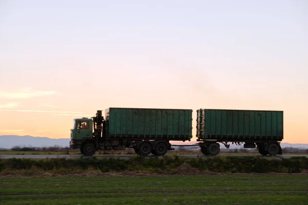 Полу-грузовик с грузовым прицепом едет по шоссе, перевозя грузы вечером. Концепция транспортировки и логистики — стоковое фото