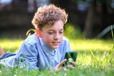 Yaz parkında akıllı telefonuyla oyun oynayan genç bir çocuk. Elektronik cihazlar konseptinden bağımlılık