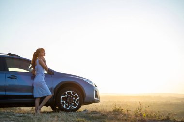 Genç bayan sürücü arabasının yanında dinleniyor sıcak yaz akşamının tadını çıkarıyor. Seyahat ve kaçış konsepti
