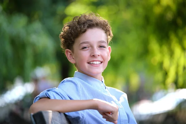 Young happy child boy relaxing sitting on bench in summer park. Positive kid enjoying summertime outdoors. Child wellbeing concept — Stock Photo, Image