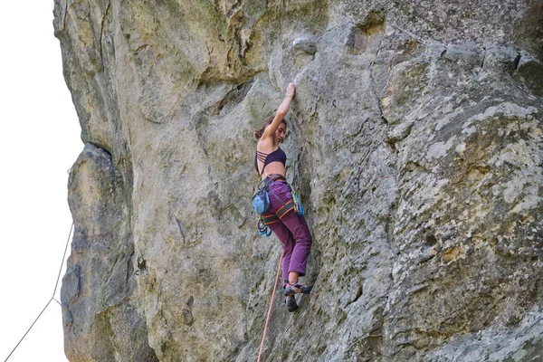 若い女性岩の山の急な壁を登る。登山家は困難な道を克服します。極端なスポーツの概念に従事 — ストック写真