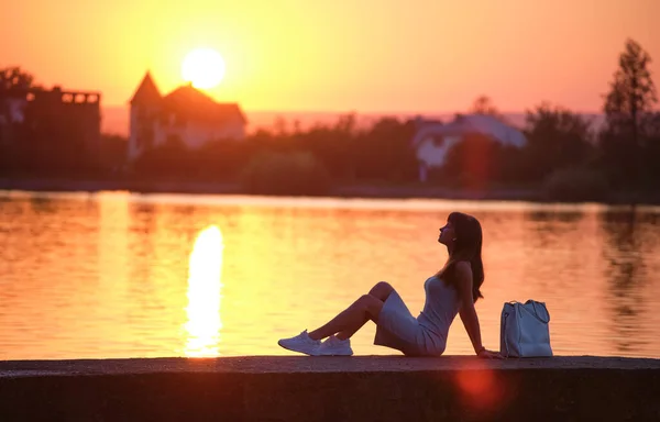 Young woman in casual outfit relaxing on lake side on warm evening. Summer vacations and travelling concept — Stock Photo, Image