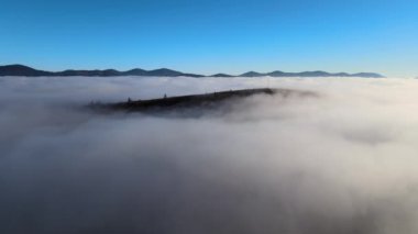 Ufuktaki dağ tepelerinin uzak karanlık siluetleri ile beyaz yoğun sis üzerinde renkli gün doğumunun havadan görüntüsü