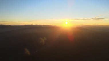 Gün batımında gün batımında parlak güneş ışınlarıyla karanlık dağ tepelerinin havadan görünüşü. Akşamları sisli tepeler ve sisli vadiler