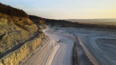 Kazı makineleri ve çöp kamyonlarıyla inşaat endüstrisi için kumtaşı malzemelerinden oluşan açık maden manzarası. Madencilik ve kullanışlı mineral üretiminde ağır ekipman