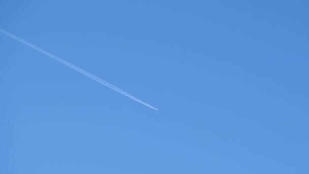 Avião de passageiros distantes voando em alta altitude no céu azul claro deixando vestígios de fumaça branca de contrail para trás. Conceito de transporte aéreo — Vídeo de Stock