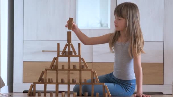 Happy child girl playing game stacking wooden toy blocks in high pile structure. Hand movement control and building computational skills concept — Stock Video