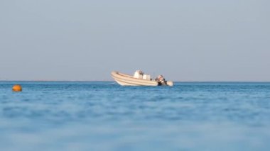 Mavi deniz suyunun dalgalı yüzeyi ve durgun dalgalarda yüzen beyaz sürat teknesiyle deniz manzarası.