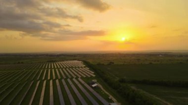 Günbatımında temiz elektrik enerjisi üretmek için birçok sıra güneş fotovoltaik paneli bulunan sürdürülebilir büyük elektrik santralinin havadan görünüşü. Sıfır emisyon kavramı ile yenilenebilir elektrik