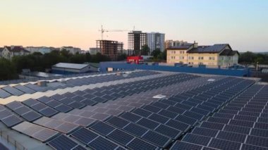 Günbatımında yeşil ekolojik elektrik üretmek için endüstriyel bina çatısına monte edilen mavi fotovoltaik güneş panellerinin hava görüntüsü. Sürdürülebilir enerji konsepti üretimi