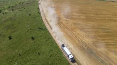 Tarım buğday tarlaları arasında toprak yolda giden kargo kamyonunun hava görüntüsü çok toz yapıyor. Hasat mevsiminde hasatçıların topladığı tahıl naklinden sonra.