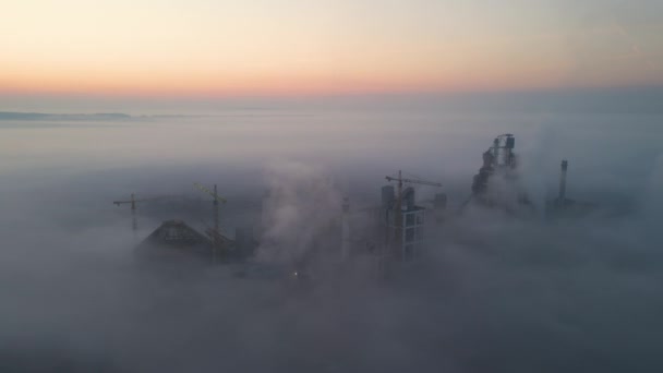 雾天晚上，在工业生产现场，高混凝土厂房结构和塔式起重机的水泥厂空中景观。生产和全球工业概念 — 图库视频影像