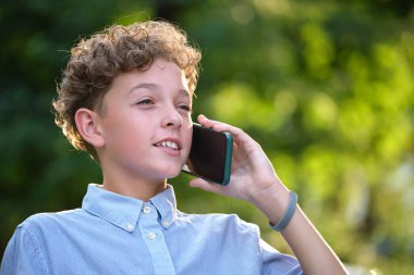Yazlık parkta cep telefonuyla konuşan mutlu genç bir çocuk. Çevrimiçi arkadaşlık kavramı