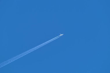 Mesafeli yolcu jet uçağı açık mavi gökyüzünde yüksek irtifada uçarken ardında beyaz duman izi bırakıyor. Hava taşımacılığı kavramı