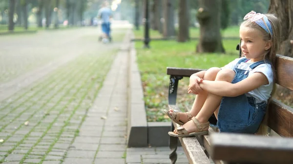 Küçük kız yaz parkında bankta tek başına oturuyor. — Stok fotoğraf