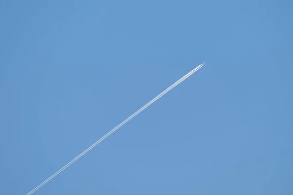 Avión a reacción de pasajeros a distancia volando a gran altitud en el cielo azul claro dejando rastro de humo blanco de la estela detrás. Concepto de transporte aéreo —  Fotos de Stock