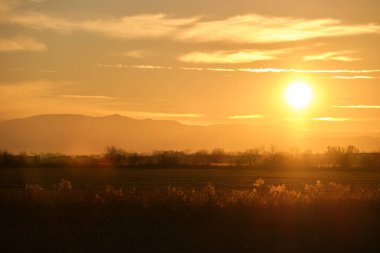 Güzel bir akşam panoramik manzarası. Gün batımında güneş batarken uzak dağ tepeleri ve asfalt yolda batıyor.