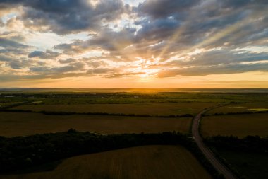 Gün batımında tarlalar arasında hızlı giden arabalarla şehirlerarası yol manzarası. Akşamları otoban trafiğinin insansız hava aracı görüntüsü