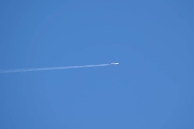 Mesafeli yolcu jet uçağı açık mavi gökyüzünde yüksek irtifada uçarken ardında beyaz duman izi bırakıyor. Hava taşımacılığı kavramı
