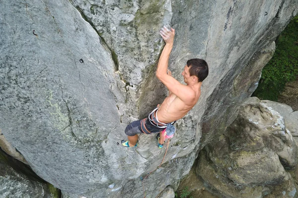 Young man climbing steep wall of rocky mountain. Male climber overcomes challenging route. Engaging in extreme sport concept — Stock Photo, Image