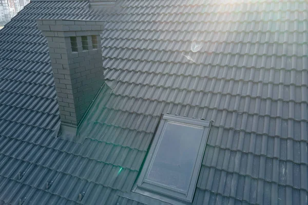 Closeup of attic window and brick chimney on house roof top covered with ceramic shingles. Tiled covering of building — Stockfoto