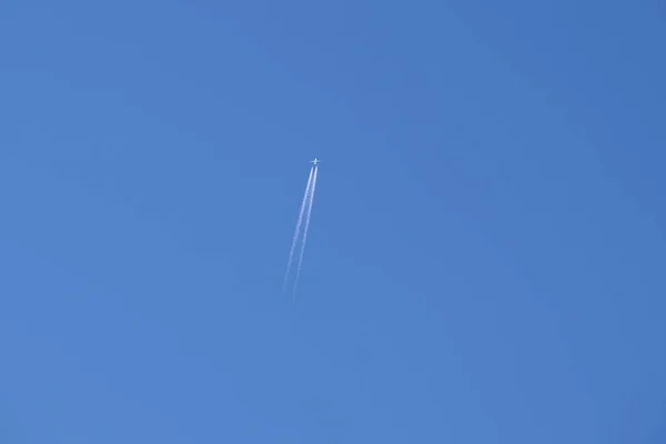 Avión a reacción de pasajeros a distancia volando a gran altitud en el cielo azul claro dejando rastro de humo blanco de la estela detrás. Concepto de transporte aéreo — Foto de Stock