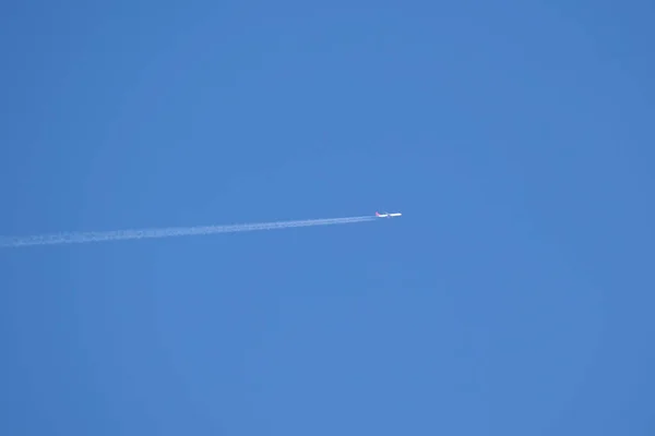 Avión a reacción de pasajeros a distancia volando a gran altitud en el cielo azul claro dejando rastro de humo blanco de la estela detrás. Concepto de transporte aéreo —  Fotos de Stock