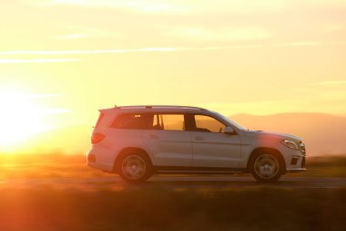 Gün batımında şehirlerarası yolda hızla giden bir SUV arabası. Akşamları otoyol trafiği