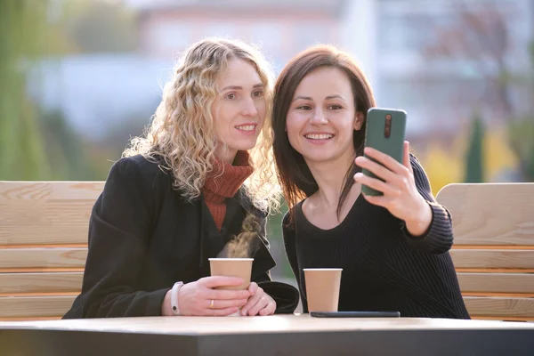 Namoradas alegres tomando selfie com sellphone descansando no café da rua da cidade. Amigos do sexo feminino curtindo o tempo juntos ao ar livre no dia quente — Fotografia de Stock