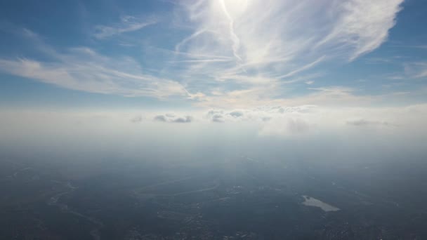 Vista aérea da janela do avião em alta altitude da cidade distante coberta com camada de névoa enevoada fina e nuvens distantes — Vídeo de Stock