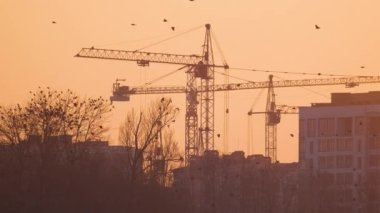 Gün batımında yüksek apartmanlı inşaat alanındaki vinçlerin koyu renkli silueti. Gayrimenkul geliştirme