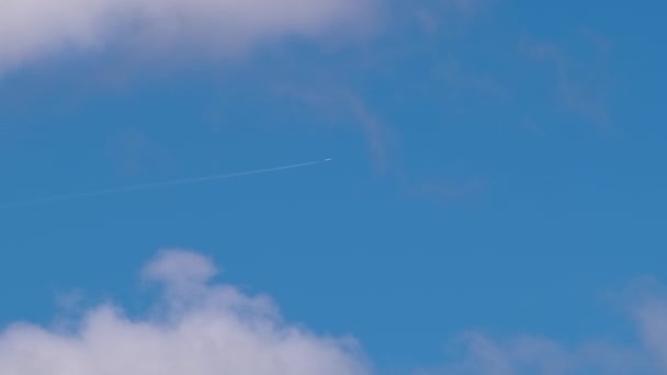 Avião de passageiros distantes voando em alta altitude no céu azul com nuvens brancas deixando vestígios de fumaça de contrail para trás. Conceito de viagem aérea — Vídeo de Stock