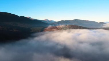 Ufuktaki dağ tepelerinin uzak karanlık siluetleri ile beyaz yoğun sis üzerinde renkli gün doğumunun havadan görüntüsü